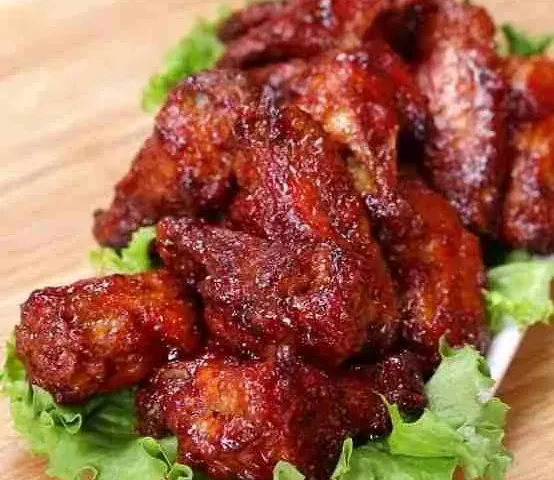 Sayap ayam bakar bumbu barbeku berwarna merah tua di atas daun selada