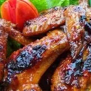 Sayap ayam bakar mengilap dengan potongan tomat dan lalapan